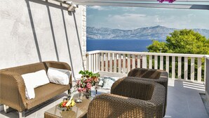 A balcony with wicker furniture, a glass table with fruit, and a view of the sea and mountains. - Amazing home in Postira (Postira)