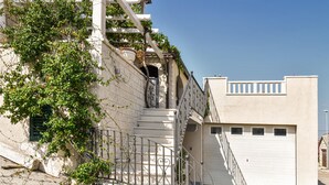 A building with a white facade, a staircase with a metal railing, and a garage door. - Amazing home in Postira (Postira)