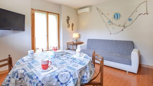 A dining area with a table set for two, a grey sofa, and a wall-mounted TV. - Nice apartment in Lido di Camaiore (Lido di Camaiore)