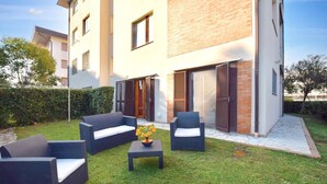 An outdoor seating area with wicker furniture and a small table, surrounded by a well-maintained lawn and a building with brick and white walls. - Nice apartment in Lido di Camaiore (Lido di Camaiore)