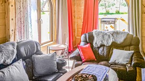 Interior acogedor de una cabaña con un sofá de cuero, una mesa de comedor de madera y vistas al exterior a través de amplias ventanas.