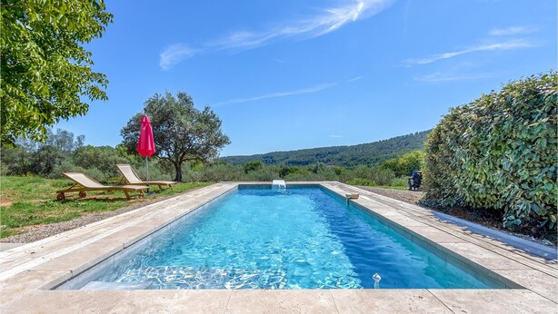 A rectangular swimming pool with a wooden deck and lounge chairs, surrounded by greenery and hills. - Amazing home in Salernes (Salernes)