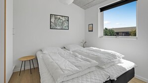 Een slaapkamer met een bed, een klein krukje, een raam met uitzicht op gebouwen, en twee wanddecoraties.