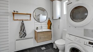 Een kleine wasruimte met een wasmachine, droger en een wasbak met een houten wastafelmeubel.
