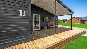 Een houten chalet met een veranda, nummer 11, een deur, een bankje en een kleine boom.