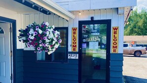 Un petit bâtiment avec une pancarte « Bienvenue », une autre indiquant « Clés » et une composition florale suspendue.