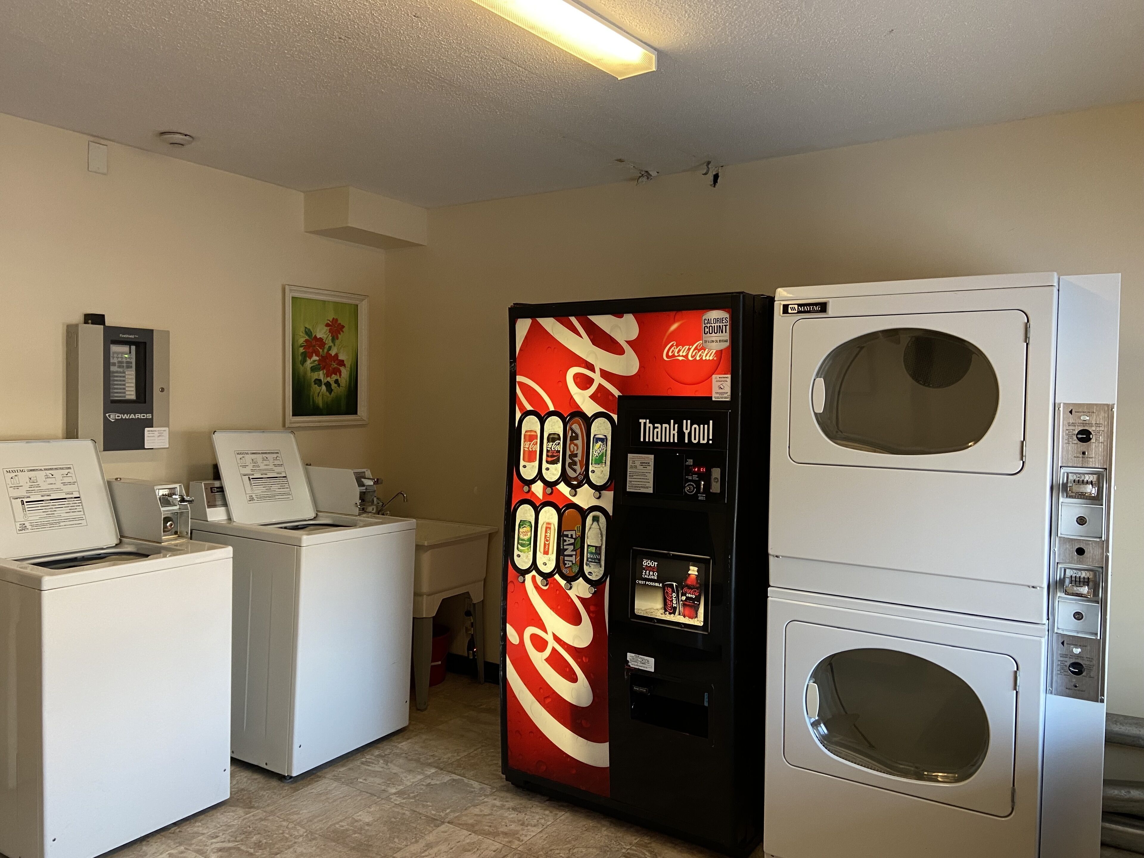 A laundry room with two washing machines, a dryer, and a Coca-Cola vending machine.