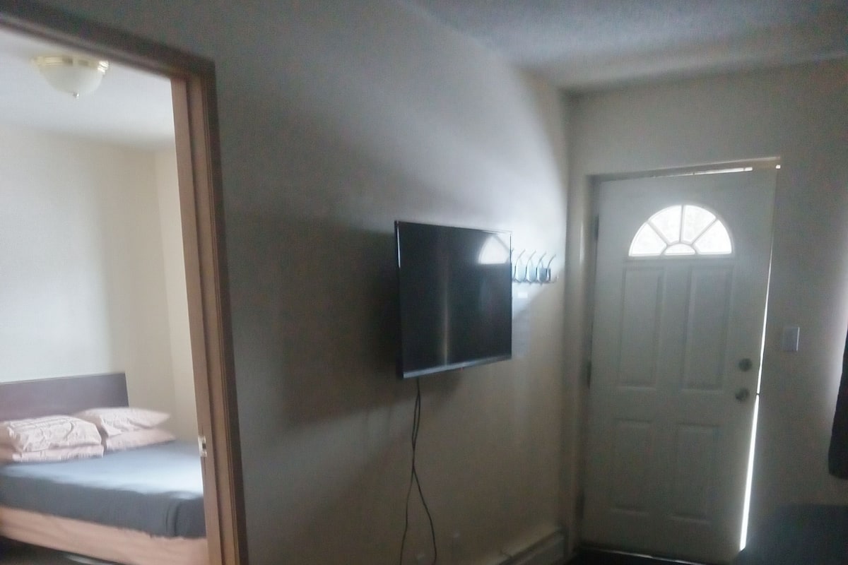 A room with a bed, a television mounted on the wall, and a door with a window.