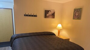 Une chambre d’hôtel comprenant un lit, une table de chevet avec une lampe, un porte-manteau fixé au mur et deux tableaux encadrés.