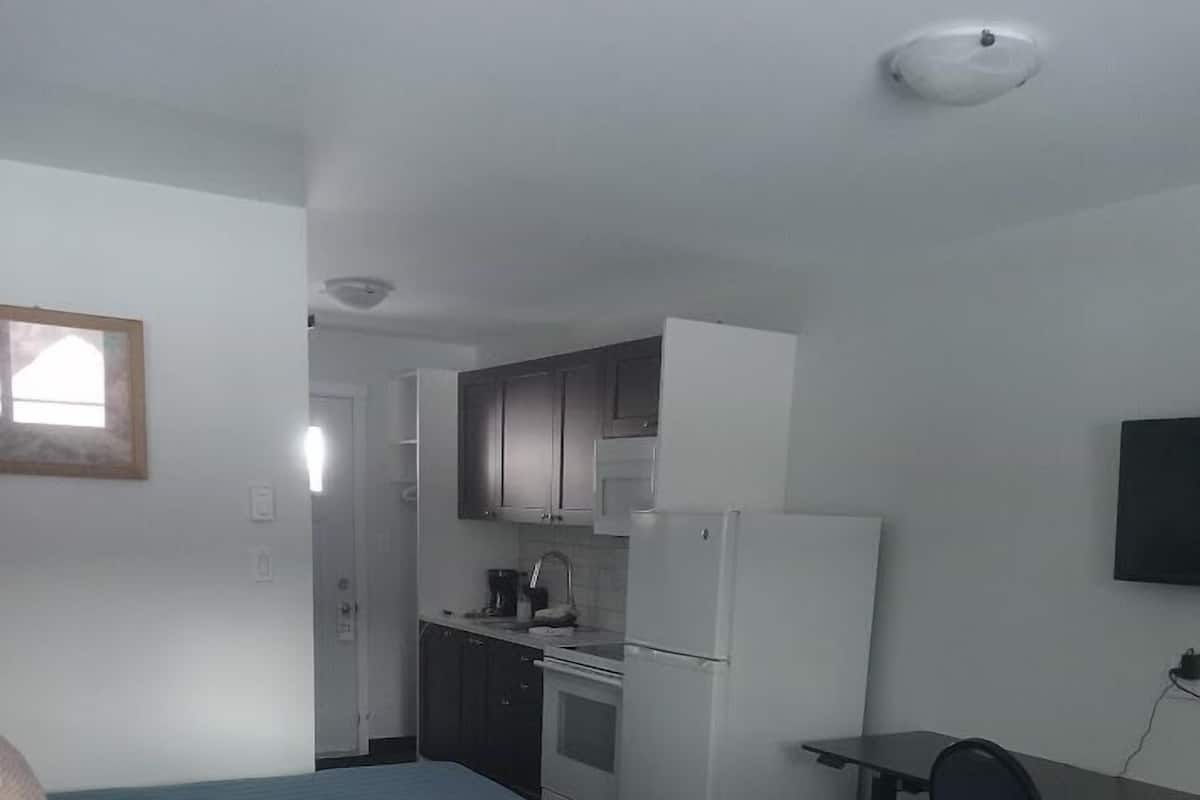 A room with two beds, a kitchenette, and a desk with a chair.