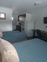 Una habitación con dos camas, una kitchenette y un escritorio con silla.