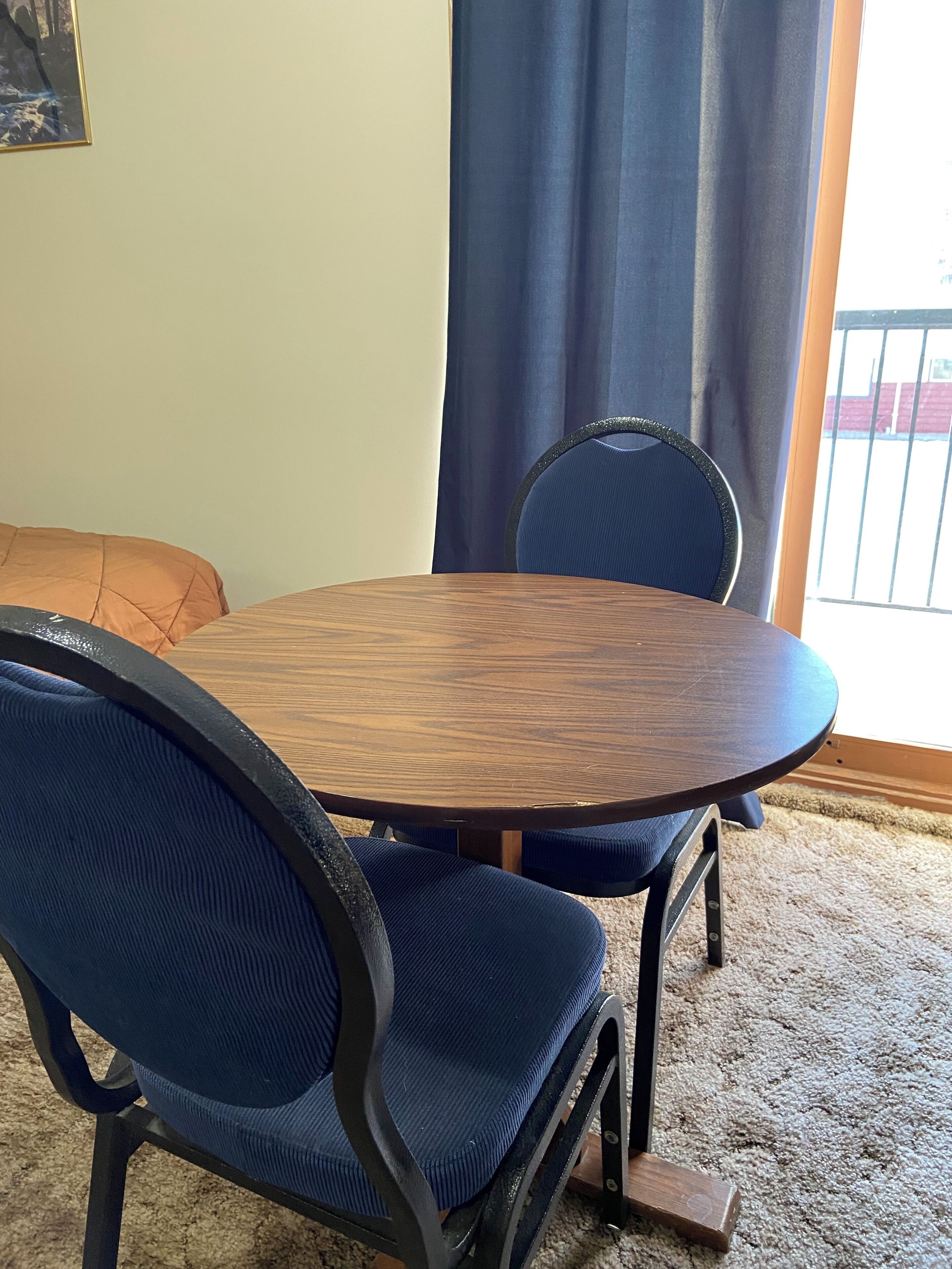 A dining area with a round wooden table, two blue upholstered chairs, and a dark blue curtain.