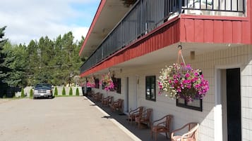 Un bâtiment à deux étages, à la façade rouge et blanche, doté d’un balcon avec des balustrades noires et de jardinières suspendues.