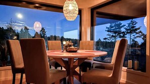 Un comedor con una mesa redonda y seis sillas, ventanas amplias con vistas a árboles y una estructura esférica distante, y una lámpara colgante.