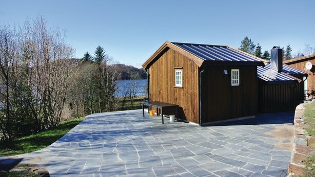 A wooden cabin with a stone patio, a small table, and a view of a lake. - Awesome home in Farsund with house sea view (Farsund)