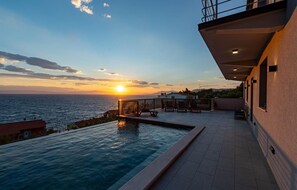 A rooftop pool with a view of the sunset over the sea, a terrace with chairs, and a building with a balcony. - Beach front home in Blato (Blato)