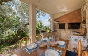 A dining area with a table set for four, a brick oven, and a view of trees.