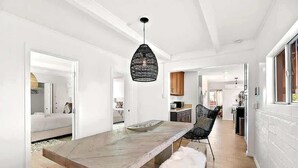 Een moderne keuken met een houten eettafel, een zwart geweven hanglamp en een witte, zachte bank.