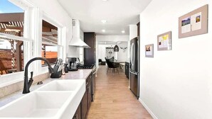 Een moderne keuken met witte kastjes, een zwarte kraan, een roestvrijstalen koelkast en een eethoek met een tafel en stoelen.