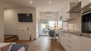 Una cocina moderna con horno empotrado, una zona de comedor con mesa y sillas, y una escalera que sube a otro nivel.