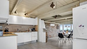 Een moderne keuken met witte kastjes, een bakstenen muur en een eethoek met tafel en stoelen.