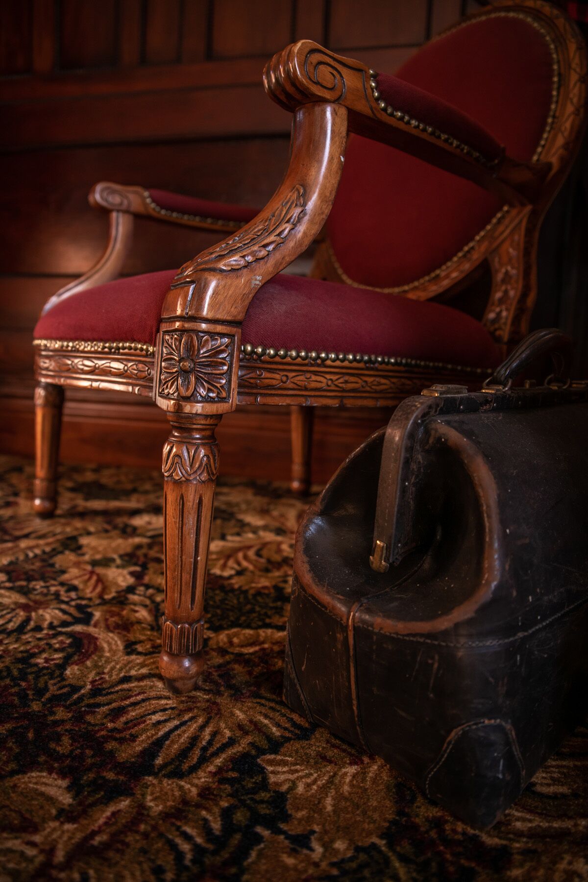 A wooden chair with intricate carvings and a red upholstered seat.