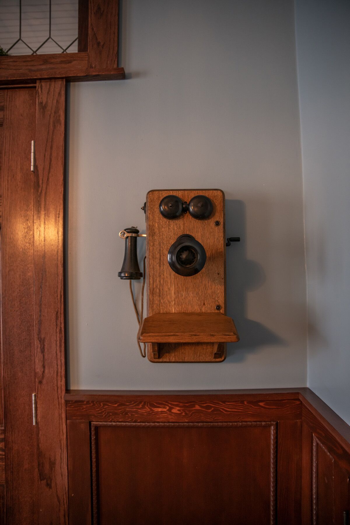 Een houten telefoon bevestigd aan een wand in een kamer met houten lambrisering.