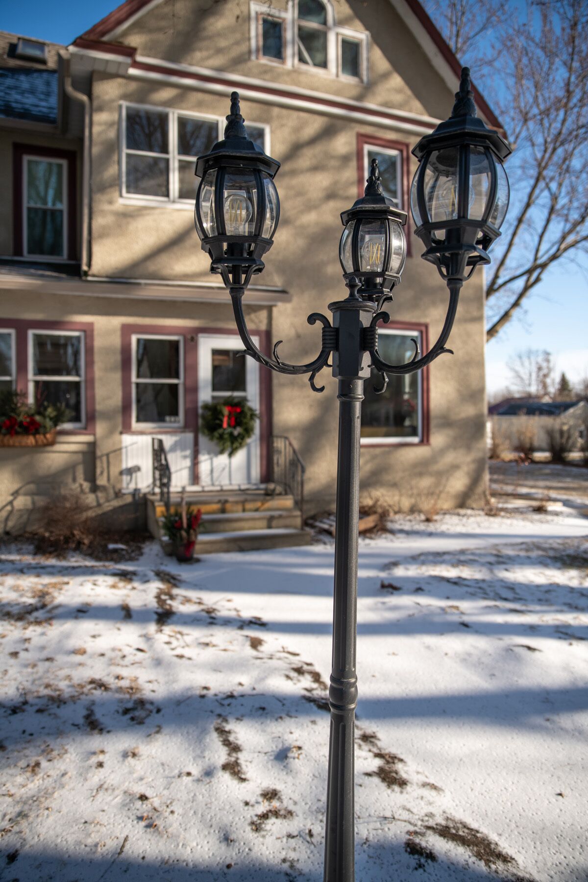 A street lamp with three lights in front of a house with a porch and a wreath on the door.