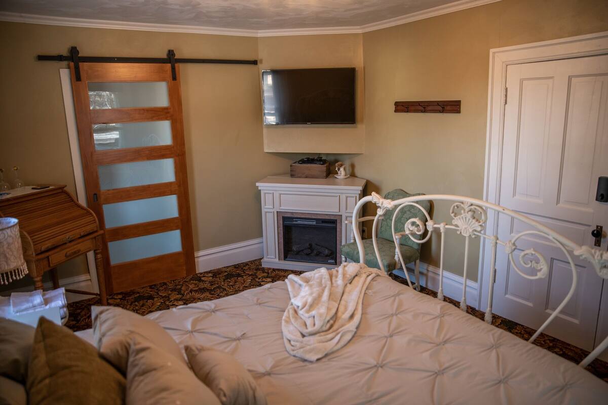 Une chambre à coucher comprenant un lit, une commode, une cheminée, un téléviseur et une porte coulissante.