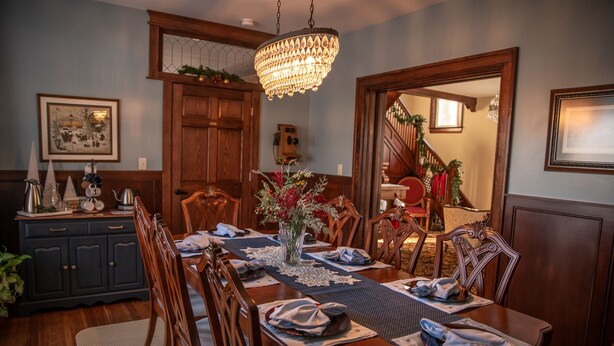Comedor con mesa de madera dispuesta para seis personas, candelabro y escalera que lleva a otra habitación.