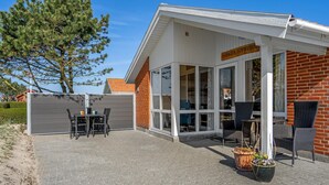 A hotel with a covered patio area featuring a table and chairs, a wicker chair, and potted plants.