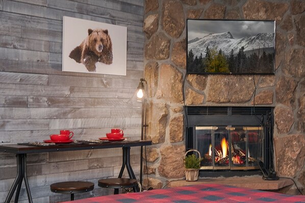 A cozy room with a stone fireplace, a table with red cups, and a bear picture on the wall.
