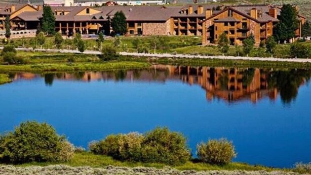 Un albergue con varias construcciones, un lago amplio y reflectante, y vegetación circundante.