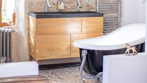 A bathroom with a stone wall, wooden vanity, a freestanding bathtub, and a mirror above the sink. - "Tilleul" Room – Indulge in understated B&B luxury (Fayence)