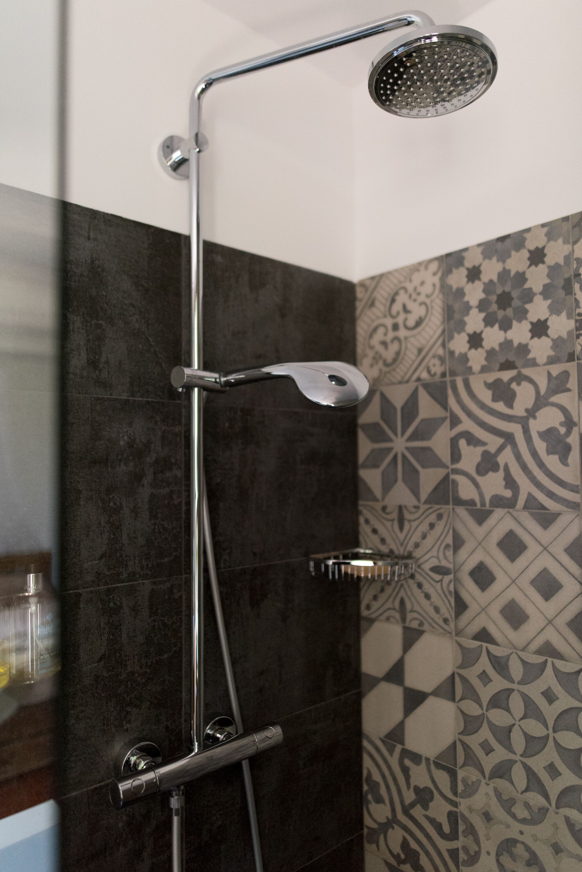 A shower with a handheld showerhead and a wall-mounted control panel.