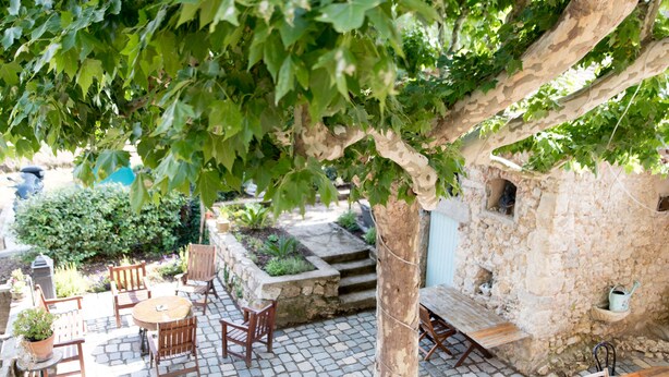 An outdoor patio with stone flooring, wooden furniture, and a tree providing shade. - "Tilleul" Room – Indulge in understated B&B luxury (Fayence)
