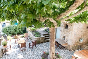 Eine Terrasse im Freien mit Steinböden, Holzmöbeln und einem Baum, der Schatten spendet.