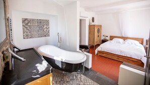 A room with a bathtub, a wooden cabinet, a bed, and a patterned wall. - "Tilleul" Room – Indulge in understated B&B luxury (Fayence)