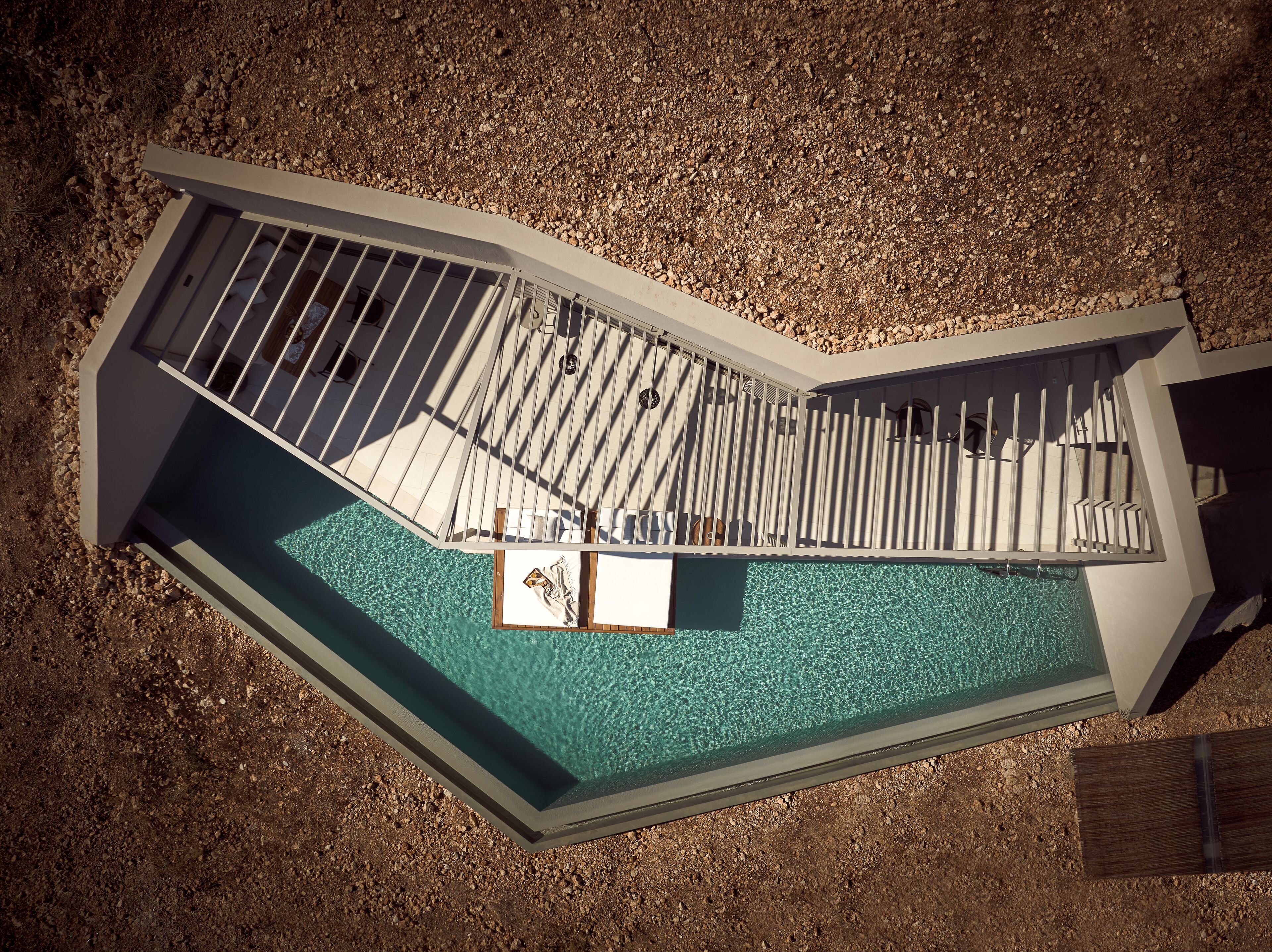 An aerial view of a swimming pool with a wooden deck and a small enclosed area with a table and chairs.