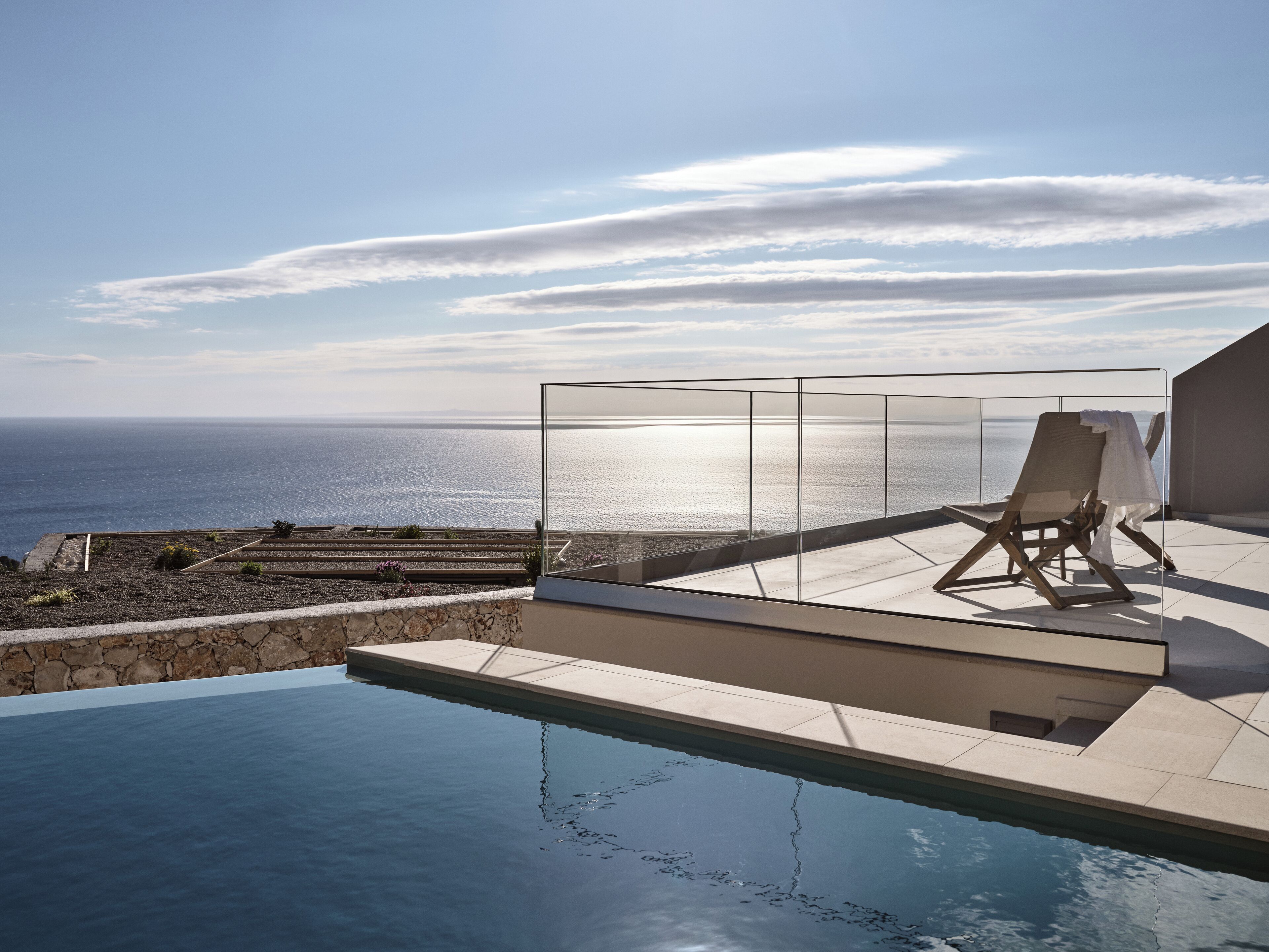 A modern infinity pool with a clear view of the ocean and a glass-enclosed lounge area with a single chair.