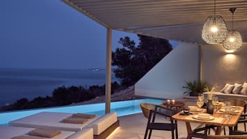 Enjoy al fresco dining with a view of the sea from this outdoor dining area, featuring a table, lounge chairs, and a stylish light fixture under a pergola.