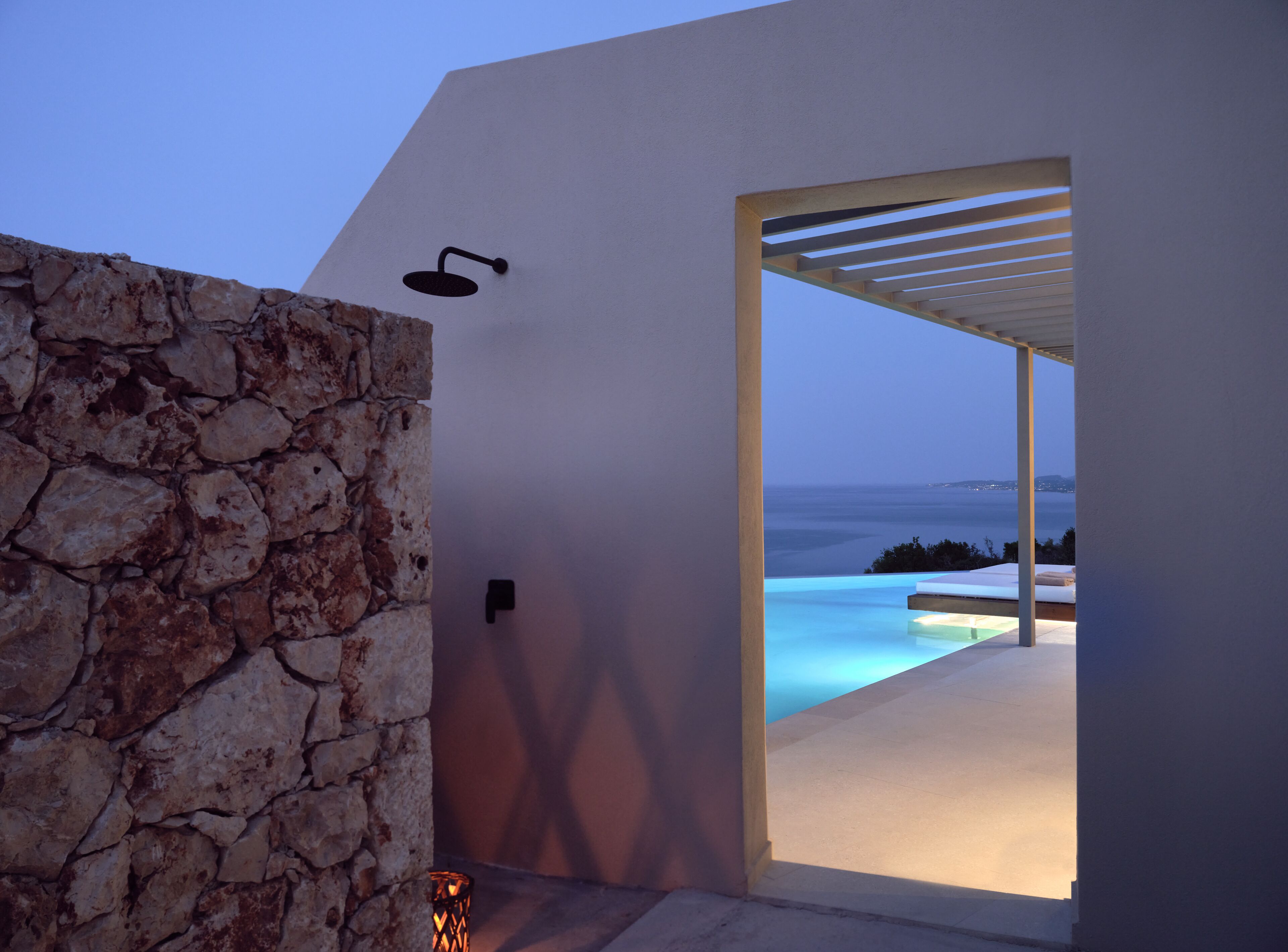 A modern outdoor area with a stone wall, a door leading to a pool, and a view of the sea.