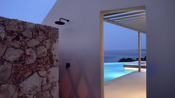 A modern outdoor area with a stone wall, a door leading to a pool, and a view of the sea.