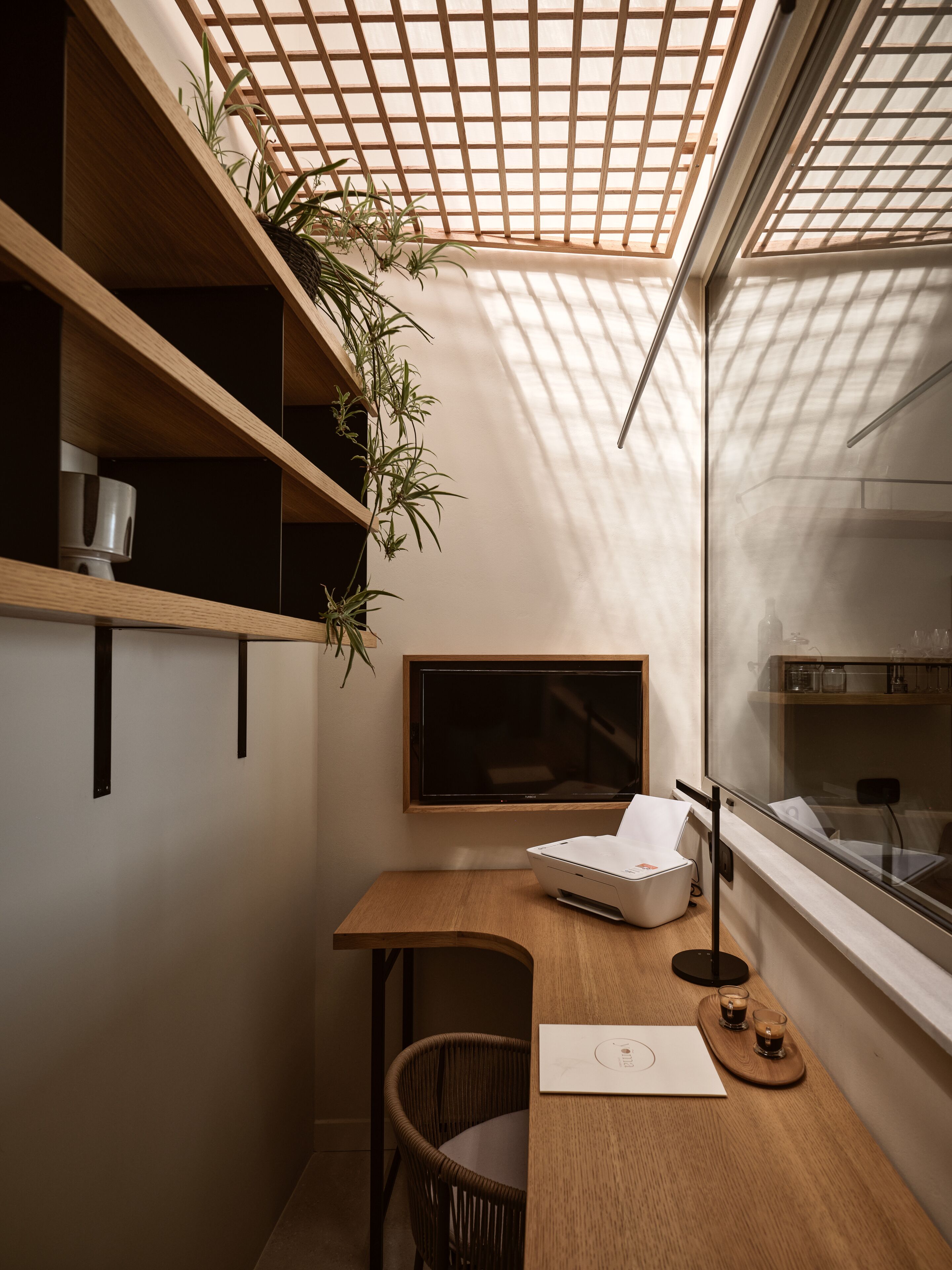 A modern workspace with a wooden desk, a chair, a large monitor, and a potted plant.