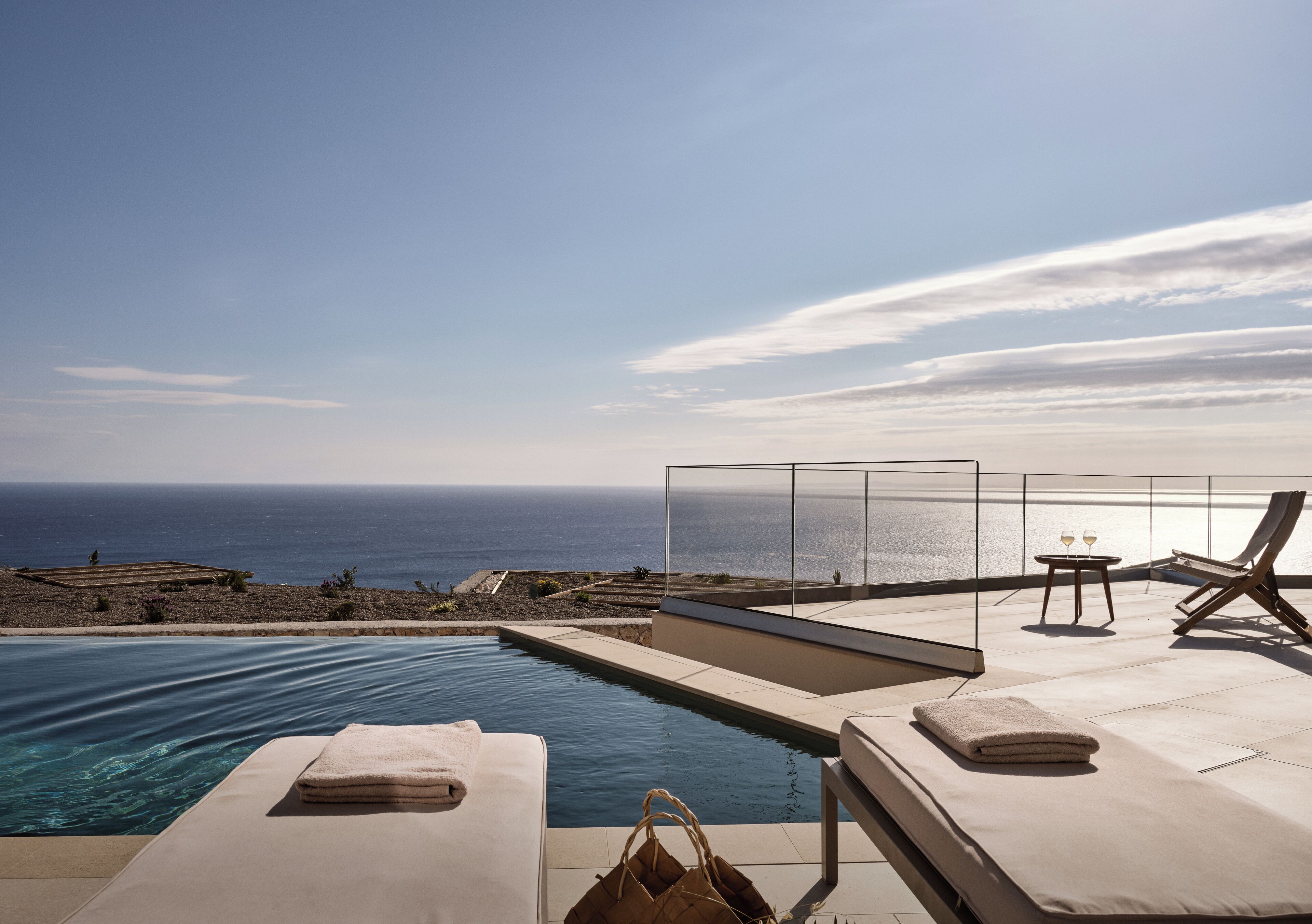 Un área junto a la piscina con sillones de descanso, un espacio de estar con paredes de vidrio y vistas al océano.