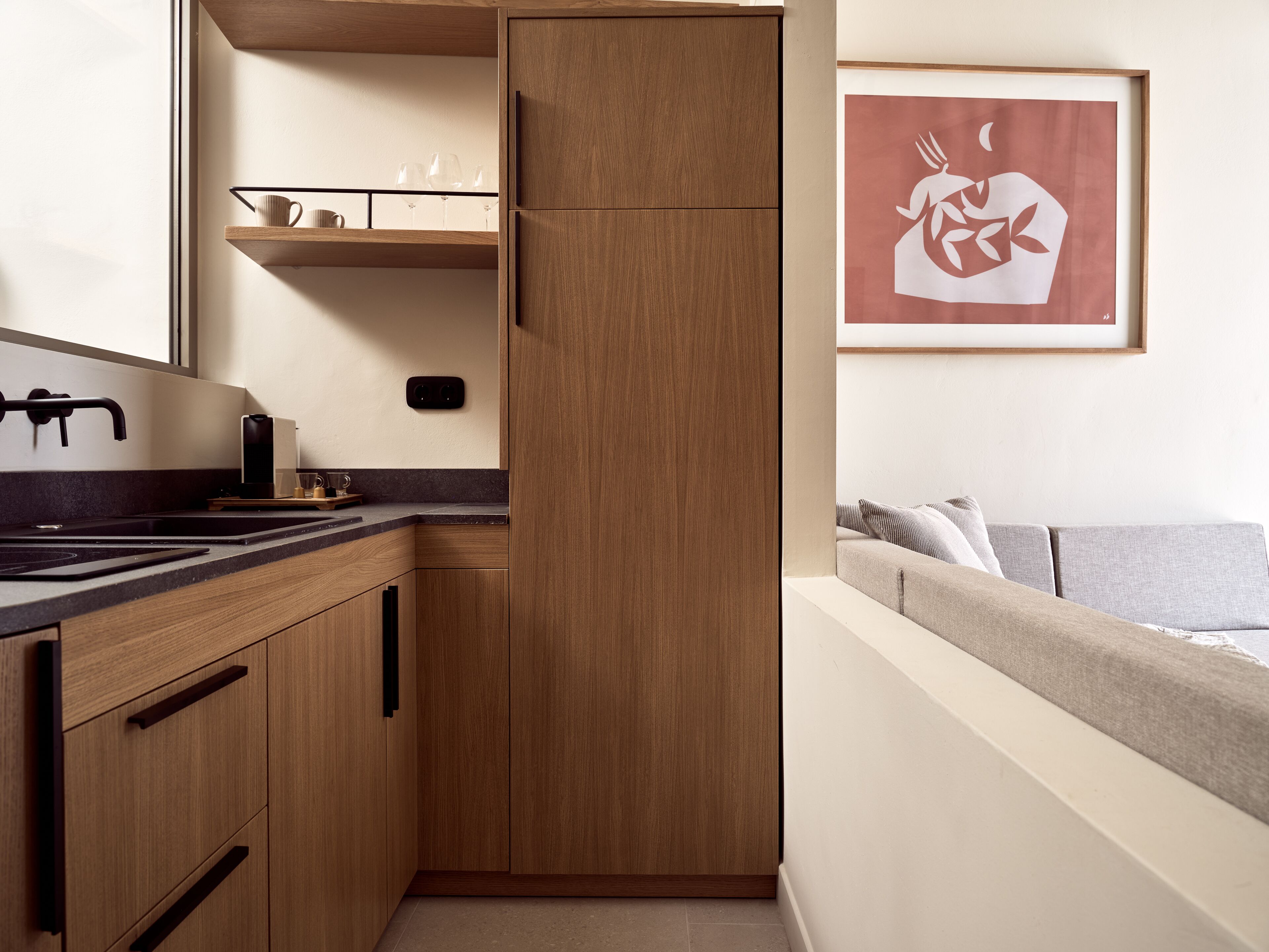 A compact kitchen with wooden cabinets, a built-in oven, and a countertop with a coffee machine.