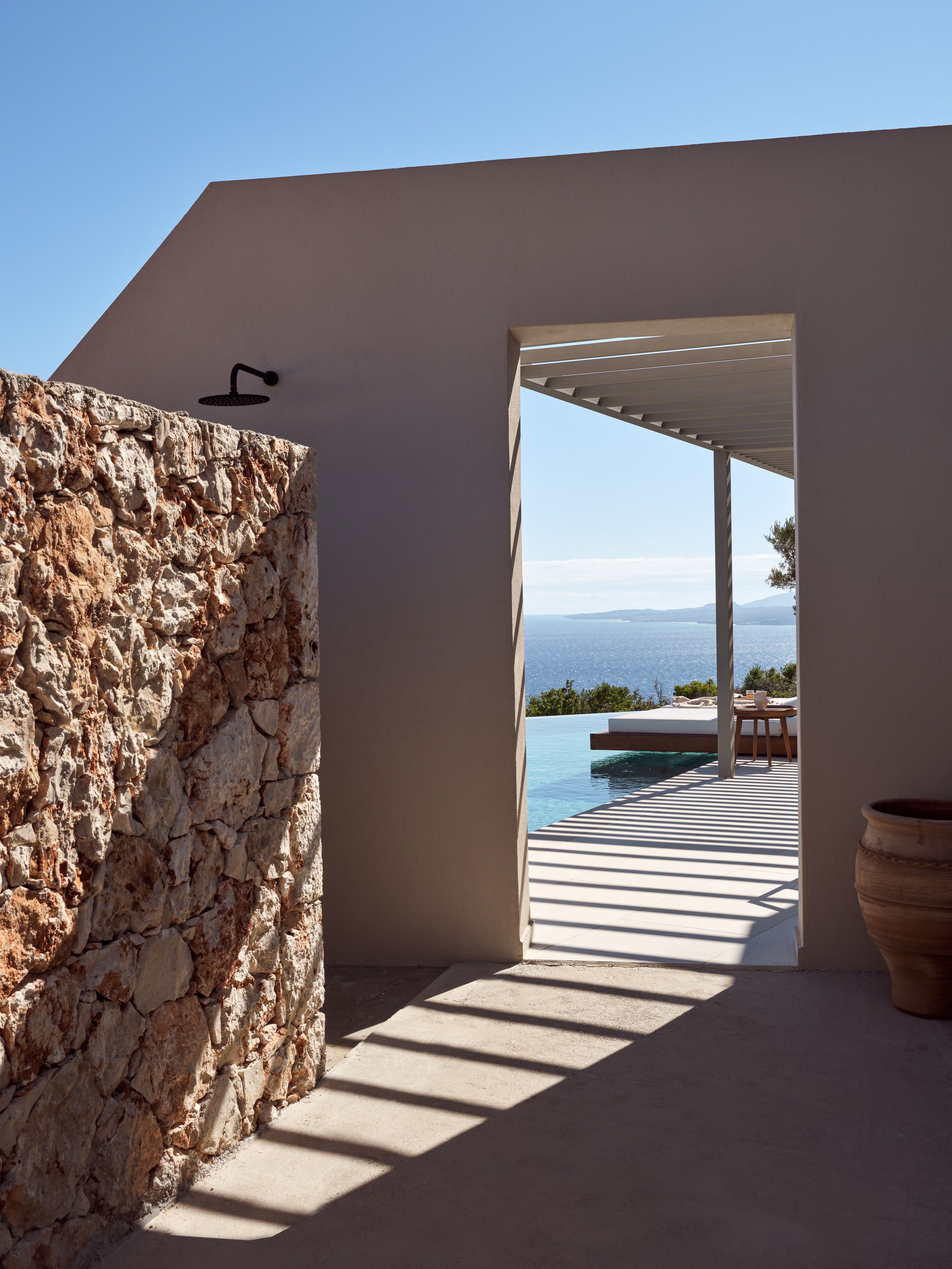 Un espacio arquitectónico moderno con una pared de piedra, vistas al mar y un patio con mesa y sillas.