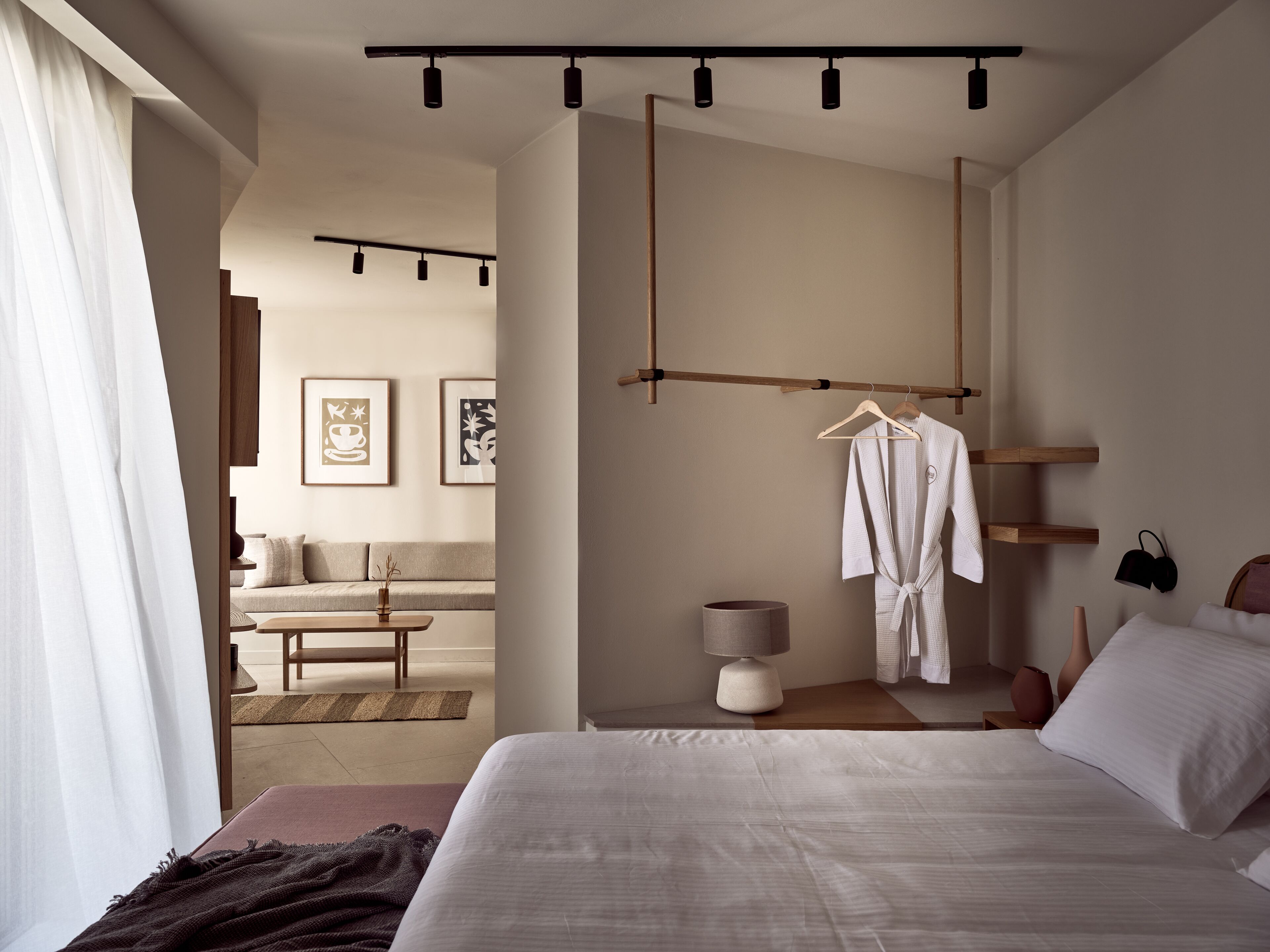 A modern bedroom with a large bed, a bedside table, a hanging robe, and a wall-mounted shelf.