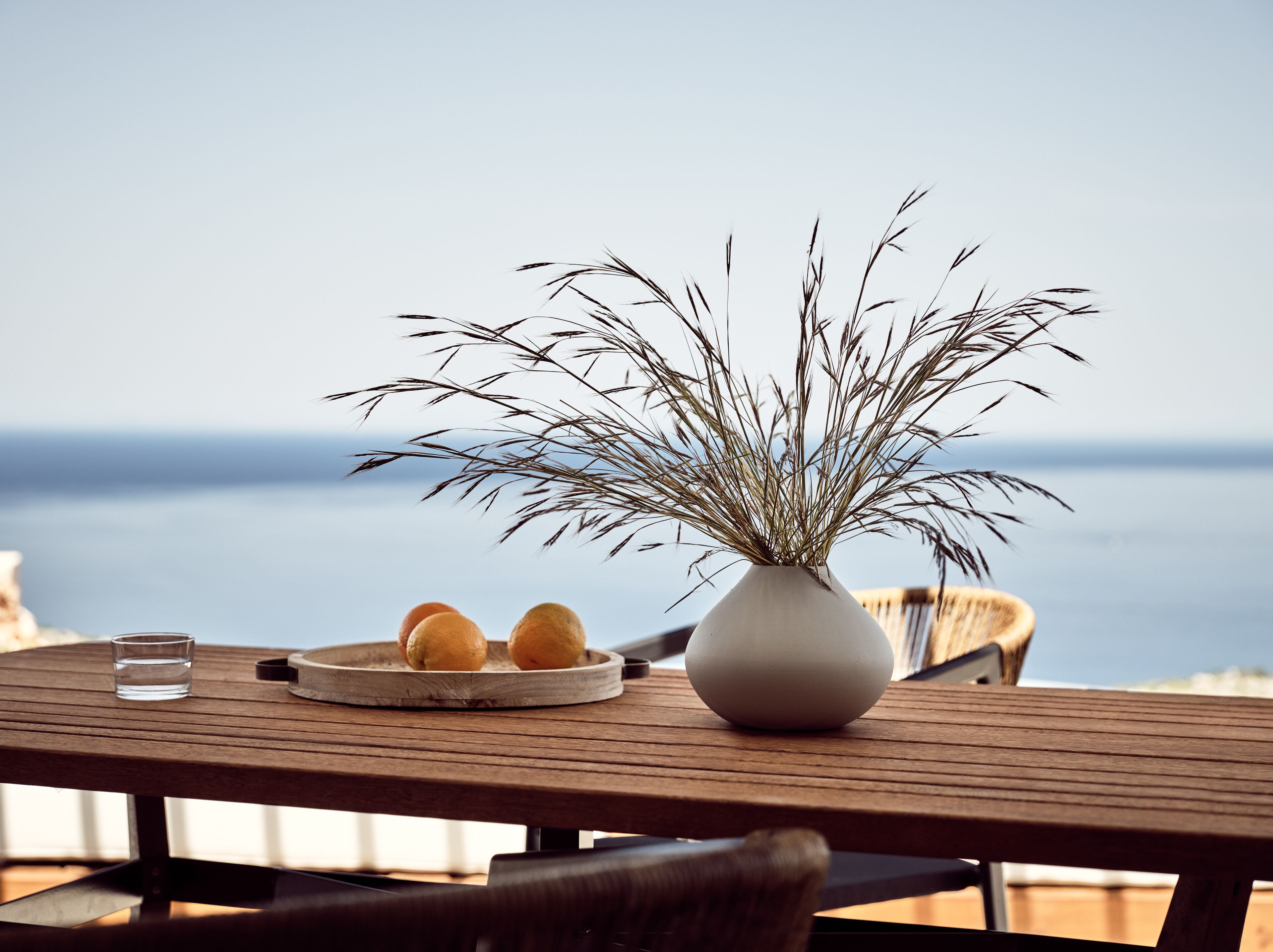 A wooden table with a white vase and a plate of lemons, overlooking a body of water.