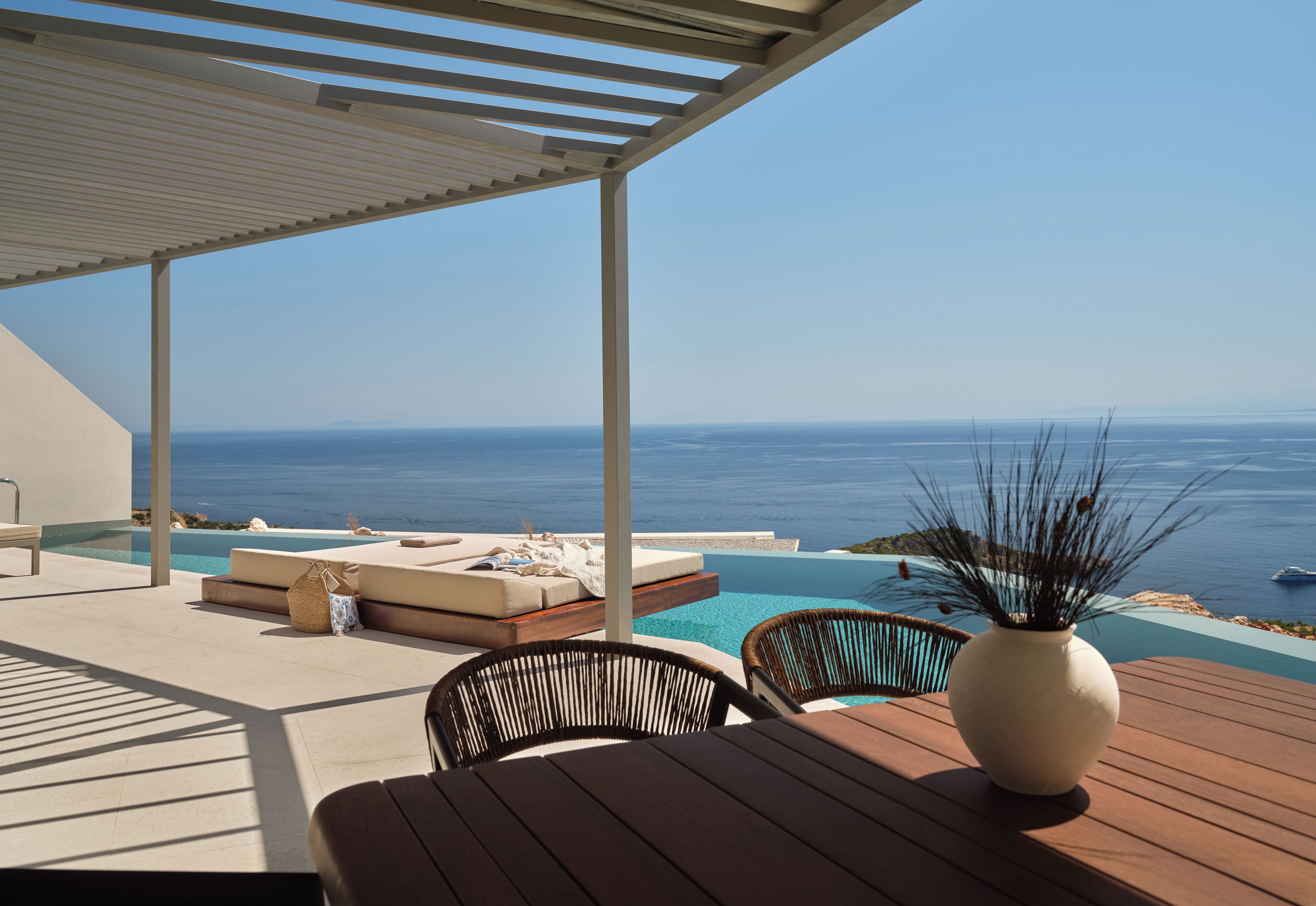 A covered outdoor seating area with a view of the ocean, a pool, and a wooden deck.